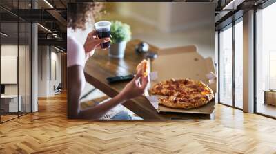 woman eating pizza and drinking cola while sitting on sofa watching tv in home late at night Wall mural