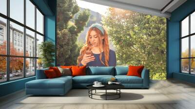 a young girl with orange hair looks at her phone under the rays of the sun Wall mural