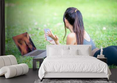 Beautiful asian girl lying down on the grass using laptop and smartphone Wall mural