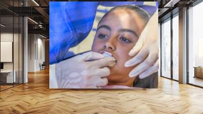 Young caucasian female with dentist in white latex gloves check condition of her teeth. baby girl in blue dental chair. Wall mural