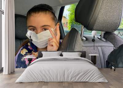 Young girl wearing mask sitting in the back of the car Wall mural