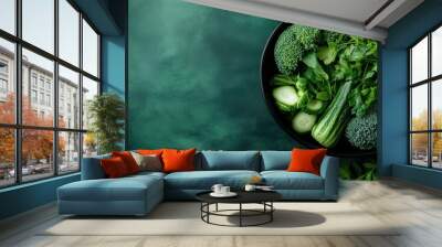 A black bowl packed with a variety of green vegetables, such as broccoli, leafy greens, cucumbers, and herbs, embodying a nutritious, appetizing, and healthy lifestyle. Wall mural