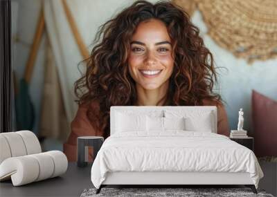 A cheerful woman with delightful curly hair smiles in a casual setting, exuding warmth and friendliness while seated in a cozy room with woven decor elements. Wall mural