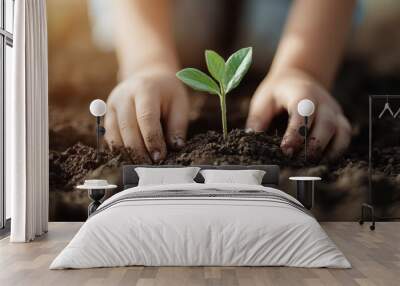 A child's hands are seen planting a small seedling in the soil, depicting an act of care and the foundational steps towards growth and nurturing in a natural environment. Wall mural