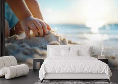 A close-up shot of a child's hand digging in the sand on a sunny beach with the ocean in the background, capturing a moment of playful exploration and innocence. Wall mural