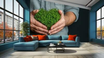 A pair of hands cups heart-shaped green foliage, contrasting against a dark surface, representing human touch and sustainability in a harmonious visual statement. Wall mural