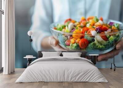 A person holds a glass bowl filled with a colorful vegetable salad, representing the freshness and healthy lifestyle choices symbolized by consuming a balanced and nutritious diet. Wall mural