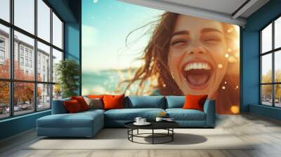 A radiant woman laughs joyfully, standing on a sunny beach with the ocean waves gently catching the warm glow of the setting sun surrounding her face. Wall mural