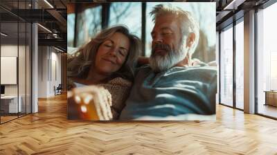 A senior couple is peacefully resting on their comfortable home couch, bathed in natural sunlight, portraying a moment of tranquility, love, and life's simple joys. Wall mural