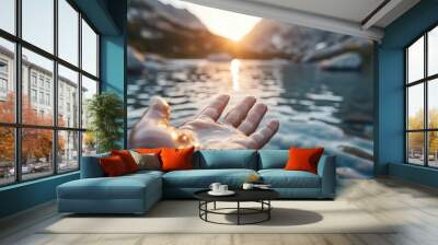 A serene image of a hand reaching towards the water at sunset over a mountainscape, evoking tranquility, hope, and the connection between nature and humans in an artistic setting. Wall mural