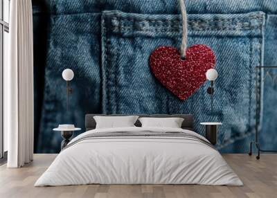 A sparkling red heart ornament dangles delicately from the tag string on a blue denim pocket, symbolizing love and fashion in a captivating visual contrast. Wall mural