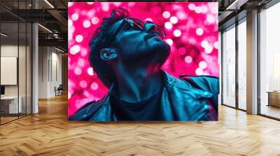 A stylish man in sunglasses and leather jacket looks upward surrounded by vibrant pink lights, capturing a modern and edgy urban vibe in a dynamic composition. Wall mural