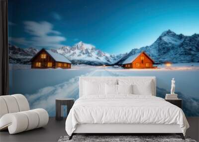 Two wooden cabins in a snowy landscape with a clear path leading towards them, surrounded by majestic mountains under a tranquil starry night sky with a warm glow. Wall mural