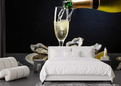 A bottle of champagne being poured into a glass of champagne on a plate with oysters on a b Wall mural