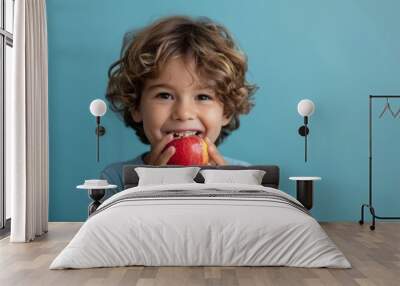 A boy holding and eating a fresh ripe apple Wall mural