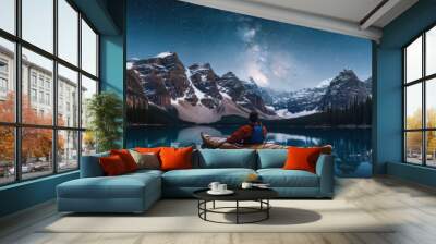 A person kayaking in lake water in winter with snow mountain and milky way starring night sky Wall mural