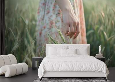 Closeup view of hand of a beautiful female touching green young wheat ear in field. Wall mural