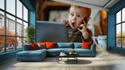 Surprised cute baby working on laptop and making phone calls at home. Remote work concept. Funny. Wall mural