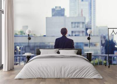 Businessman standing on open balcony watching city view. Business ambition and vision concept.the view from the back Wall mural