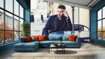 Fashionable man in a jacket sits at a table in the street Wall mural