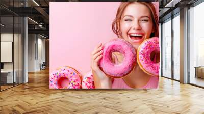 Happy woman holding two tasty pink donuts on pink background Wall mural