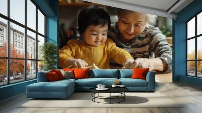 A grandmother and a baby girl are making dough together in a kitchen. Wall mural