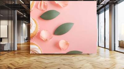 Vector illustration of cupcakes arranged in a circle with flower petals and leaves scattered on a soft pastel pink background. Wall mural