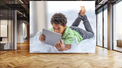 Boy teenager with tablet computer lying in bed having fun in bedrom Wall mural