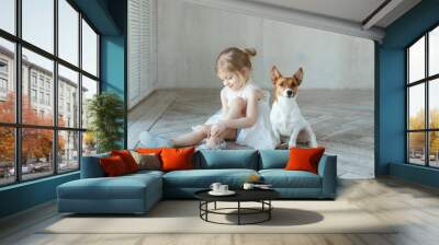 A girl sits on the floor in a room with a dog and brings the pointes Wall mural