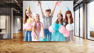 group of small children have birthday party, wear festive hats, hold balloons, have joy together, en Wall mural