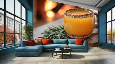 A mug of orange liquid sits on a wooden table next to some green leaves Wall mural