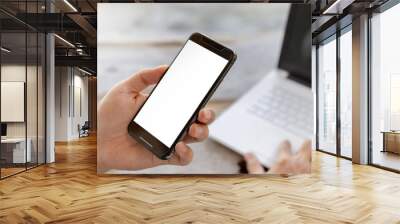 Close up of young man hand using mobile smartphone with blurred laptop background, Mockup concept. Wall mural