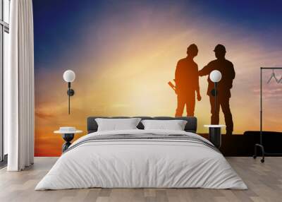 Silhouette of Engineer and worker standing on stone thinking of project sunset in evening time. Wall mural