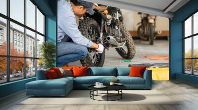 Young man fixing motorcycle in workshop garage, Man repairing motorcycle in repair shop, Mechanical hobby and repairs concepts Wall mural