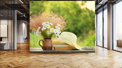 Chamomile flowers, book and summer hat on table in sunny garden. Harmony, peaceful mood, relax time. summer season concept. Rustic composition Wall mural