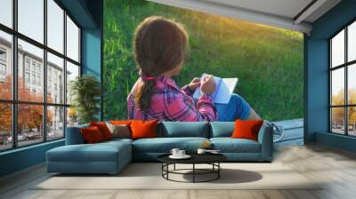 young girl sitting on bench and writing in notebook outdoor, abstract sunny natural background. Child studying in summer garden. education, writing hobby concept Wall mural