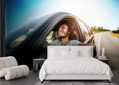 Joyful young man driving car on asphalt road Wall mural