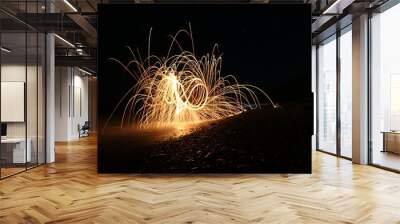 Light painting en la playa por la noche con reflejos sobre agua y piedras calidas. Chispas. Wall mural