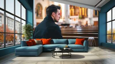 young caucasian man praying in church with blurred background - faith and religion concept Wall mural