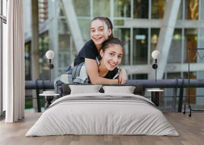 two teenage sisters in the city, one perched on the back of the other Wall mural