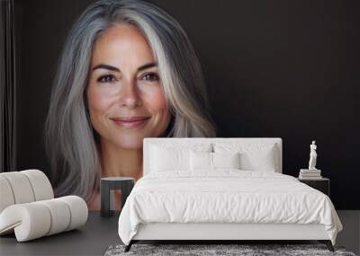 A confident older woman with gray hair smiles warmly, showcasing beauty and experience in a soft, neutral setting Wall mural