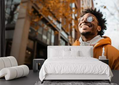 black person with glasses and afro hair looking up with yellow jacket and white sweatshirt laughing and very happy. Wall mural