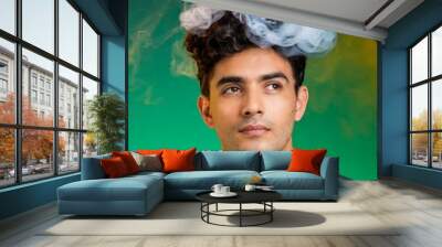 Close-up portrait of young man with smoke coming out of her head from thinking so much, isolated on bright green background Wall mural