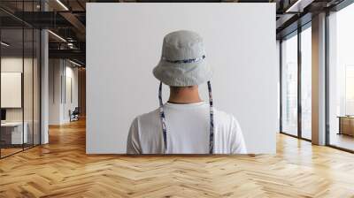 A bucket hat with a blue cord being modeled by a young man on his back. Product photo. Wall mural