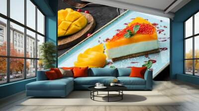 Creamy mango cheesecake decorated with red berries and mint on a large plate and dark background, close up view. Summer desserts and sweets Wall mural