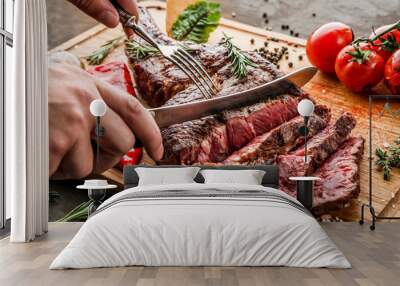 Hands cut grilled tomahawk meat medium rare or rib eye steak on wooden cutting board with grilled vegetables on dark background, close up Wall mural