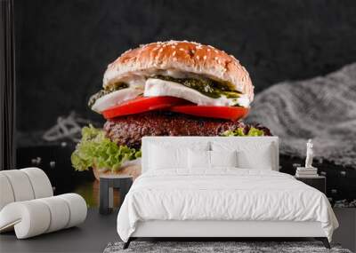 Tasty burger with mozzarella cheese, tomatoes, lettuce and sauce pesto on slate black background, close up Wall mural