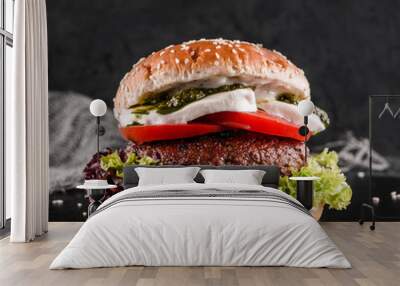 Tasty burger with mozzarella cheese, tomatoes, lettuce and sauce pesto on slate black background, close up Wall mural