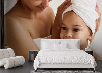 A young mother and her little daughter in white towels in the bedroom in the morning. Happy family at home. Wall mural