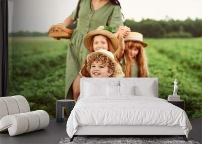 Beautiful young caucasian mother with children in a linen dress with a basket of strawberries gathers a new crop and has fun with the children Wall mural